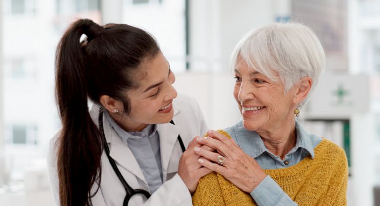 Freundliche Ärztin legt einer älteren Patientin die Hand auf die Schulter