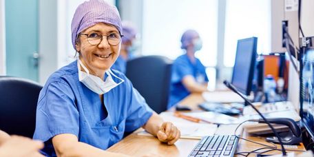 Eine Mitarbeiterin im Bereich Elektrophysiologie sitzt lächelnd an ihrem Arbeitsplatz